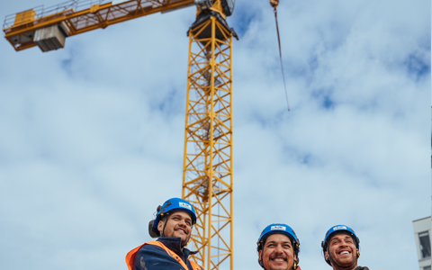 Construction workers smiling with crane in background.